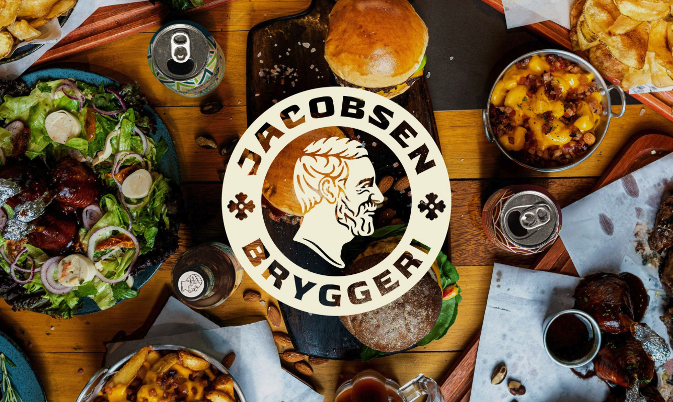 A Jacobsen Bryggeri logo is centered over a table with a burger, salad, mac and cheese, fries, a drink can, and various foods, creating an inviting, rustic vibe.